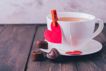 Valentine's day. Cup of tea and chocolate candies in shape hearts. Red paper heart for Message. Love or holiday concept. Copy space