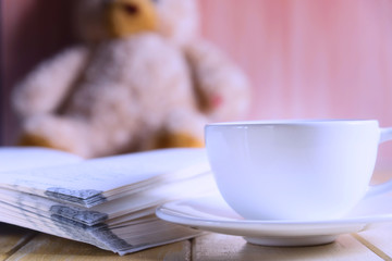 coffee cup and book focused on teddy bear in Blurred background