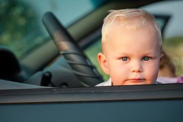 One little  boy sitting in the car and look out from the car win
