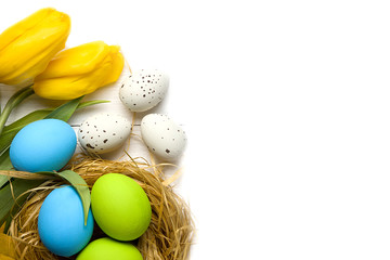 Easter card with colorful eggs in nest and yellow tulips over white background. Top view with copy space
