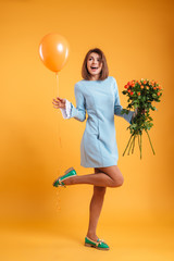 Fototapeta na wymiar Cheerful pretty young woman holding bouquet of roses and balloon
