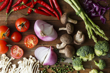 Fresh vegetable cooking ingredients on rustic wooden table with knife and brand new wooden chopping board