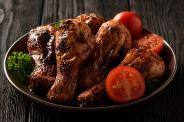 Roasted chicken legs with tomatoes on wooden background.