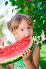 Cute little girl eating watermelon on the park in summer time. . Enjoy. Portrait.