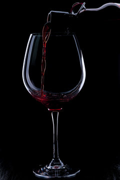 Red Wine Pouring Into A Wineglass. Isolated On Black Background.