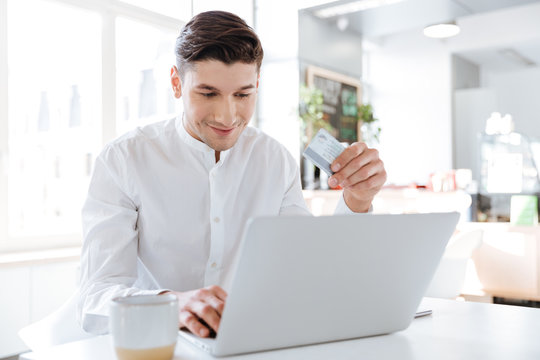 Handsome man using laptop computer holding credit card