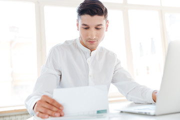 Handsome man using laptop while holding documents