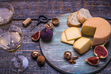 White wine in a glass, cork, bottle screw and a set of products - cheese, grapes, nuts, olives, figs on a wooden board, background