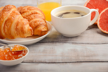 Fresh Croissants with coffee, jam and orange juice for breakfast on rustic wooden background. Copy space, horizontal.