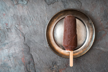 Chocolate covered popsicle in the metal plate on the stone background top view