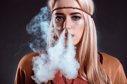 Young woman in the Boho style blowing smoke