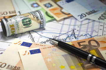 Us dollar bill and euro banknotes lying on the chart of dollar euro prices.Japanese candlesticks on the diagram. Pen on the bills. Concept of currencies trading. Selective shallow focus.
