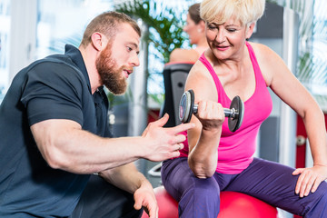 Naklejka premium senior woman working out with dumbbells with personal trainer