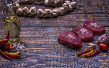 Raw Beef Steak, salt, pepper, garlic, olive oil, rosemary  on the black wooden board, background.