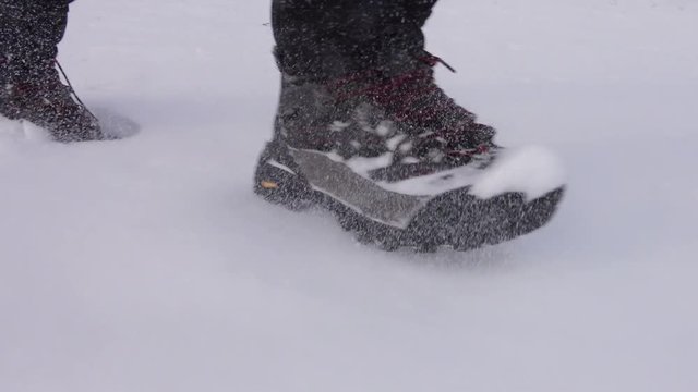 Man running in deep snow on winter day, low angle camera in motion following male feet in waterproof boots