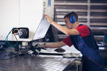 Inside a factory, industrial worker in action on metal press machine holding a steel piece ready to...