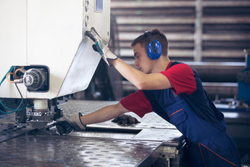 Inside a factory, industrial worker in action on metal press machine holding a steel piece ready to...