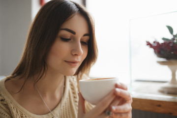 Woman typing text on smartphone in a cafe while coffee is cools