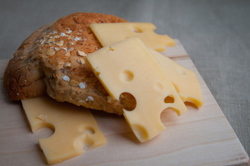 Eco food, meal, lunch concept. Sliced pieces of maasdam cheese with holes served in rustic style on a wooden board with home made bread. Close up.