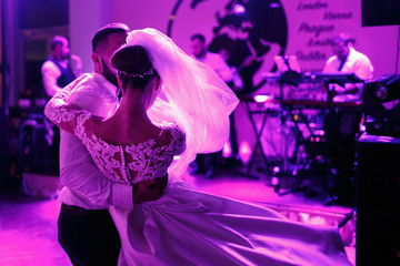 Violet lights illuminate groom whirling elegant bride in lace dr