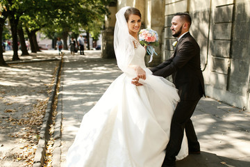 Naklejka premium Groom holds bride's waist while she triees to whirl in her magni