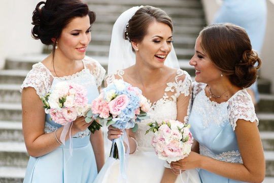 Laughing bride and bridesmaids tell funny stories standing on fo