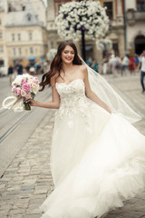 Fototapeta na wymiar Stunning brunette bride with long hair whirls on an old street