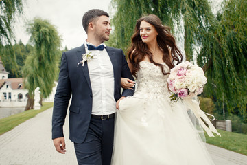 Beautiful bride with long curls holds groom's hand during a walk