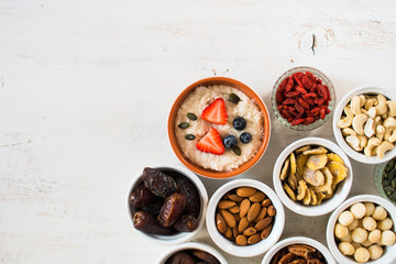 Healthy eating concept: paleo stye coconut porridge made with almond milk, topped with strawberries, various fruit and nuts on the back, selective focus