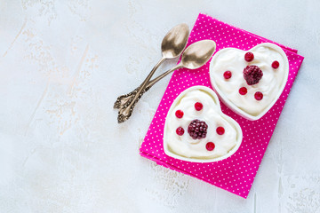 Obraz na płótnie Canvas Valentine day decoration, breakfast, yogurt with berries for two in white heart-shaped bowls on the table. Top view, flat lay.