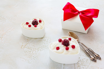 Valentine day decoration, breakfast, yogurt with berries for two in white heart-shaped bowls and gift box on the table.