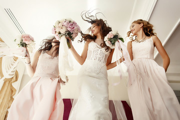 Bride and bridesmaids with wedding bouquets jump on bed in hotel