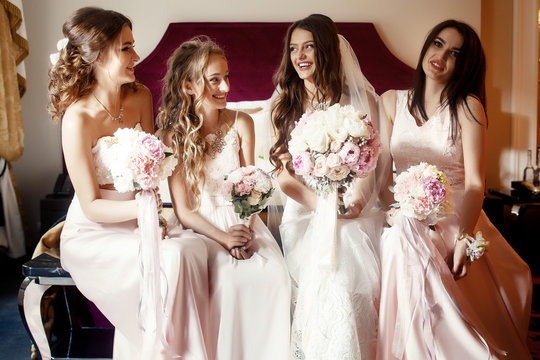 Chating bride and bridesmaids sit on soft bed in luxurious hotel