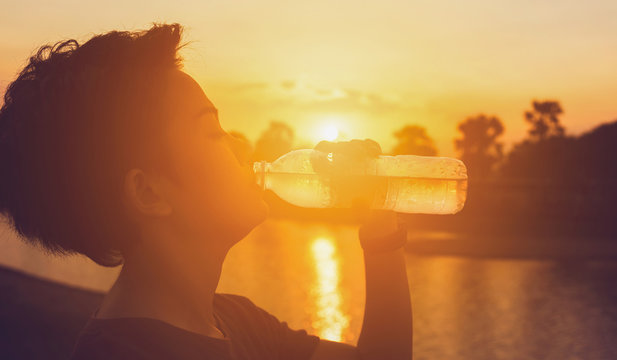 Female drinking a bottle of water on sunset
