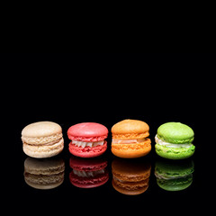 Multicolored macaroons isolated on black background with reflection. Free space for text