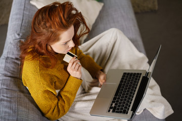 nachdenkliche frau sitzt auf dem sofa mit laptop und kreditkarte