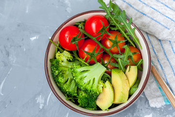 A bowl with a simple vegetable salad (broccoli, tomatoes, avocado, arugula)