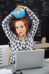 studentin sitzt am schreibtisch und hält einen globus auf ihrem kopf