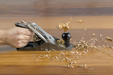 Close up of a carpenter planing a plank of wood with a hand plane.