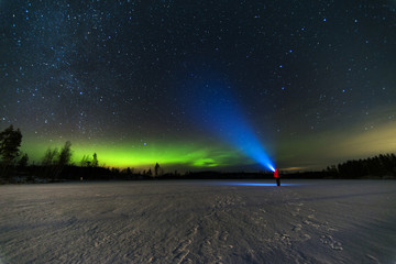 person puts bright blue flashlight to the starry sky with green north lights using torch staying on...