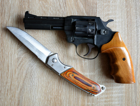 Black revolver pistol with knife on wooden board.