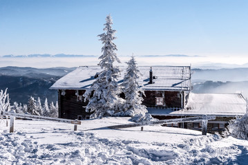 Bezrucova chata on Lysa hora hill in winter Moravskoslezske Beskydy mountains with snow, frozen trees, blue sky and Mala Fatra mountain range on the background