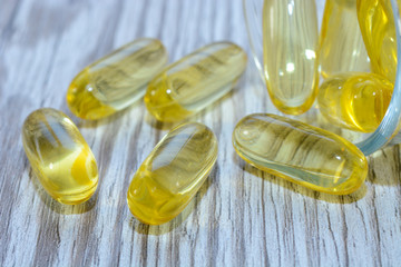 Fish oil gelatin softgels with omega 3 and vitamin D on a wooden texture with sun beams, healthy...