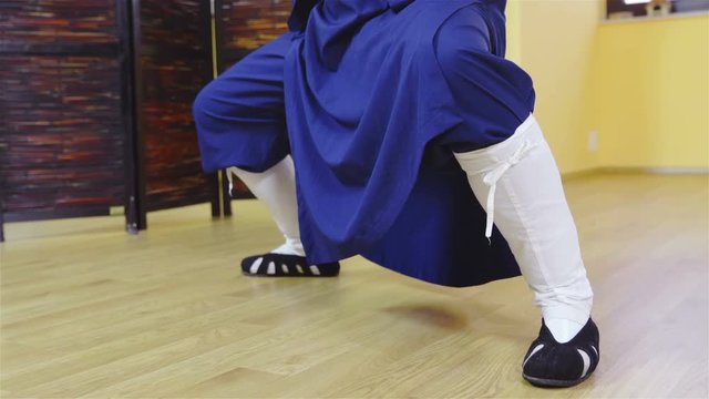 Person legs with traditional shoes in blue uniform make a squat form 4K
