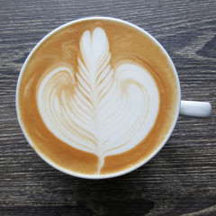 Top view of a mug of latte art coffee on timber background.