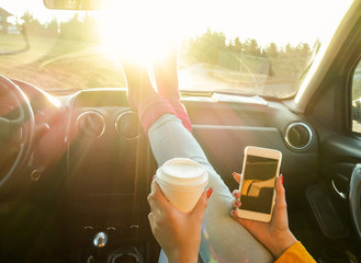 Woman toasting coffee take away go cup and using phone inside car
