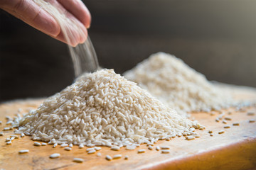 Hand pouring rice on pile of white rice on wooden table backgrou