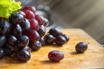 Bunch of red, black, purple grapes lay on wooden tables with lig