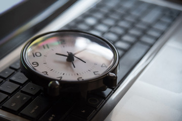 Black clock lay on keyboard time metaphor concept in dark low ke