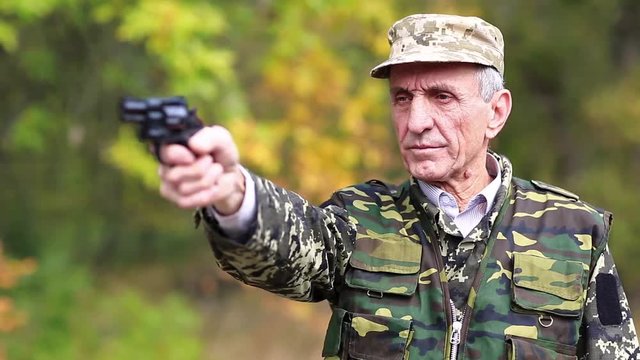 Retired officer in military uniform shoots a revolver. Man with black gun. Retired officer at shooting range. Senior man in military uniform shoots a pistol in forest